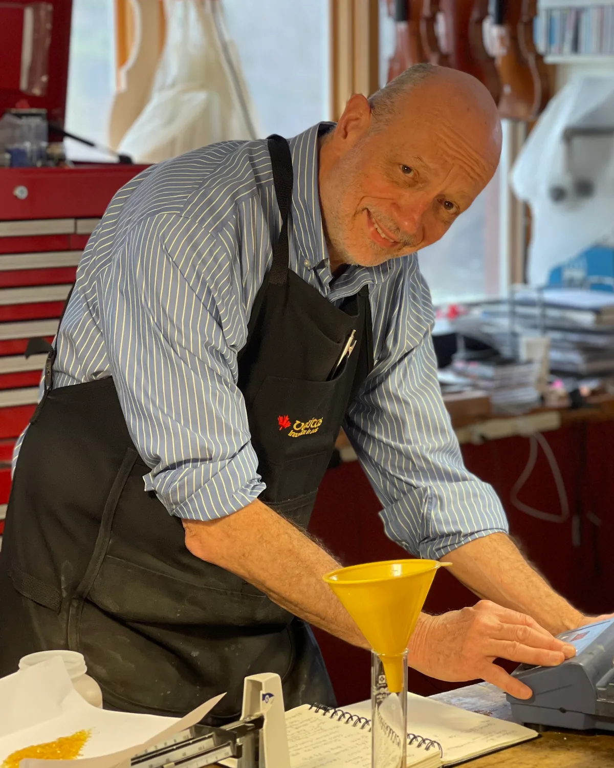 Kevin Flannery at his bench applying finish to an instrument, smiling.
