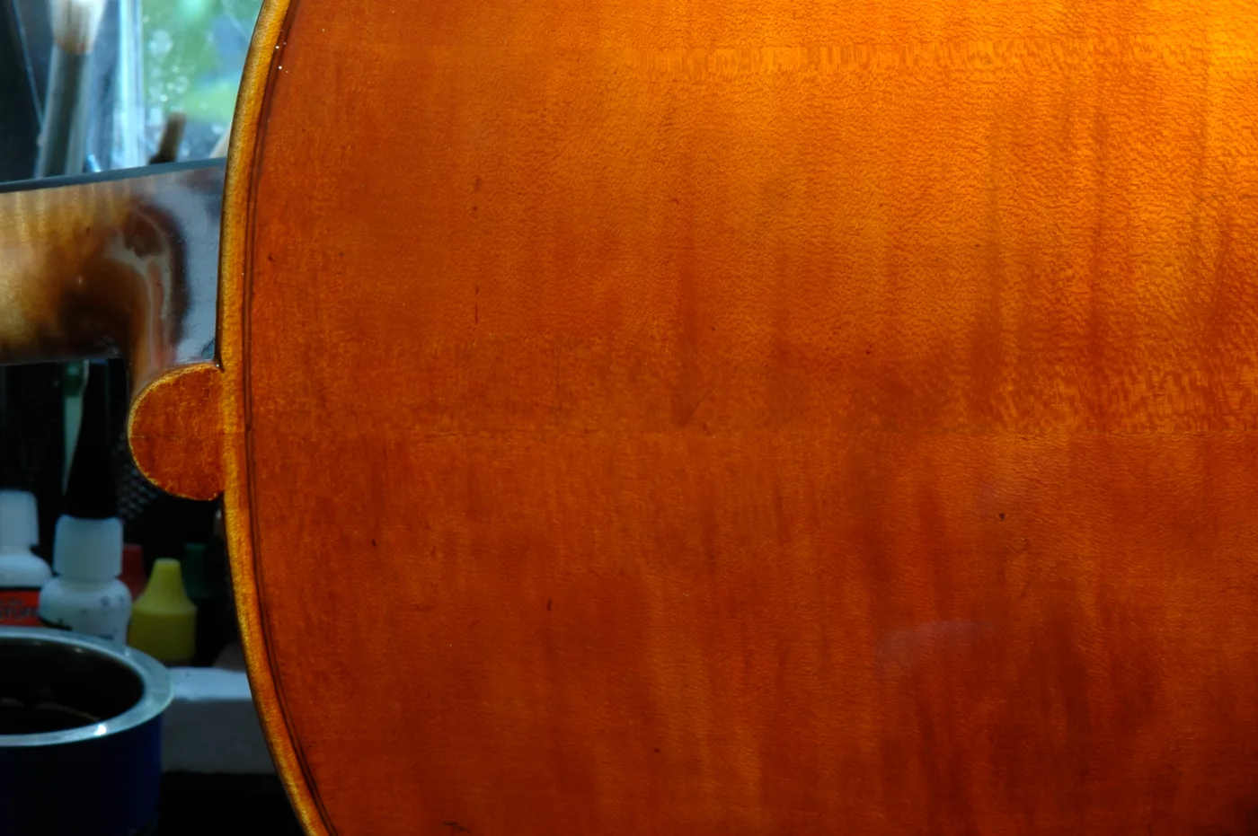 The flamed-maple back of a cello, deep varnish grain in window light.
